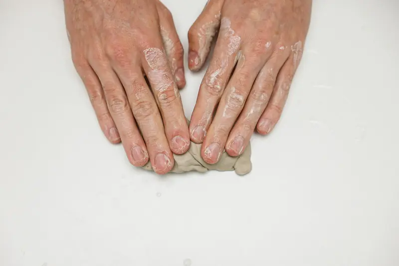 Adult hands shaping clay on a white surface during a craft project