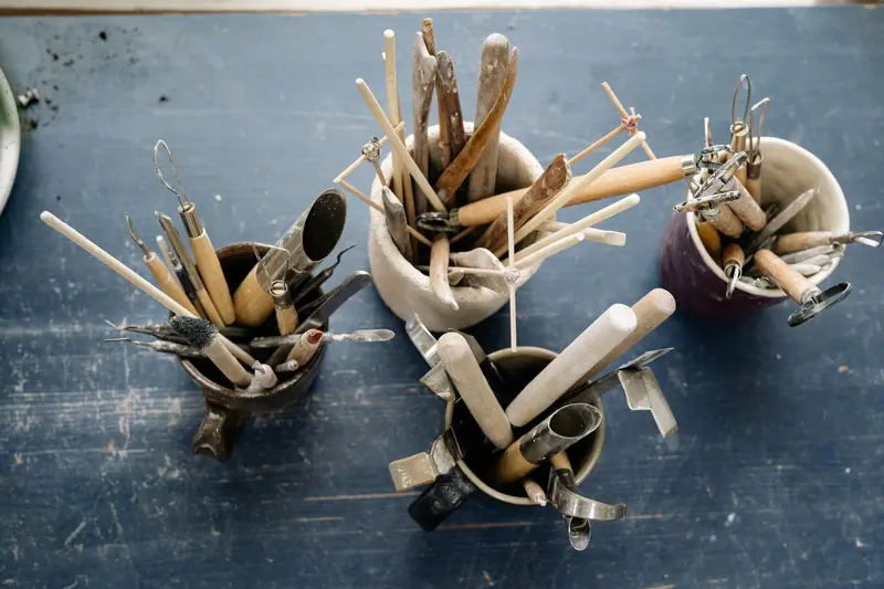 A top view of ceramic sculpting tools in mugs on a rustic wooden table, ideal for artists