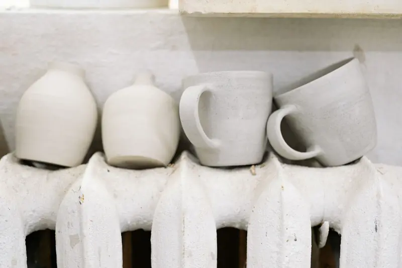Handcrafted ceramic mugs and vases drying on a radiator in a pottery studio