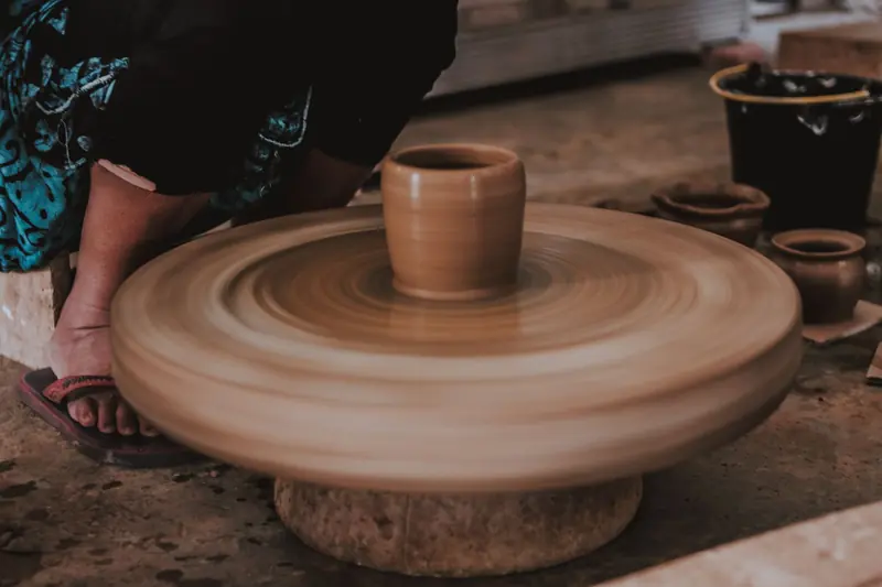 An artisan potter skillfully shapes clay on a spinning wheel, creating handmade pottery