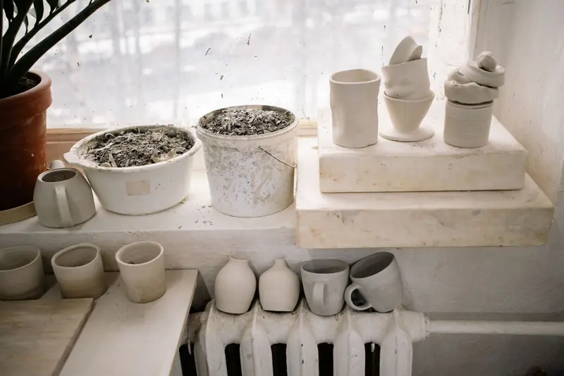A collection of handcrafted pottery cups displayed on a window sill indoors, showcasing minimalist design