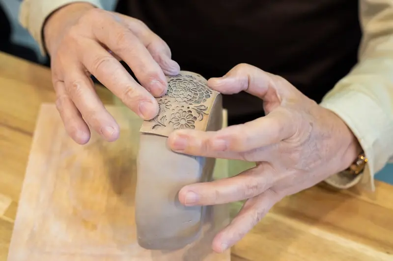 Close-up of hands molding and decorating a clay pot, showcasing craftsmanship in pottery making