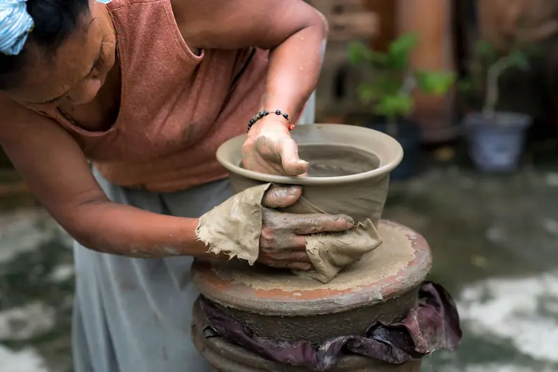 A woman skillfully molds clay into pottery on a traditional wheel outdoors