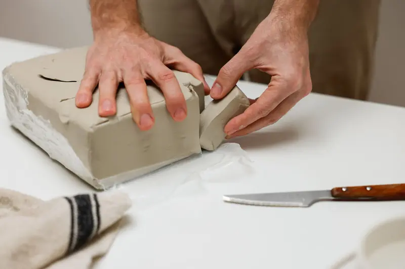 Hands shaping a clay block on a table, showcasing pottery preparation techniques