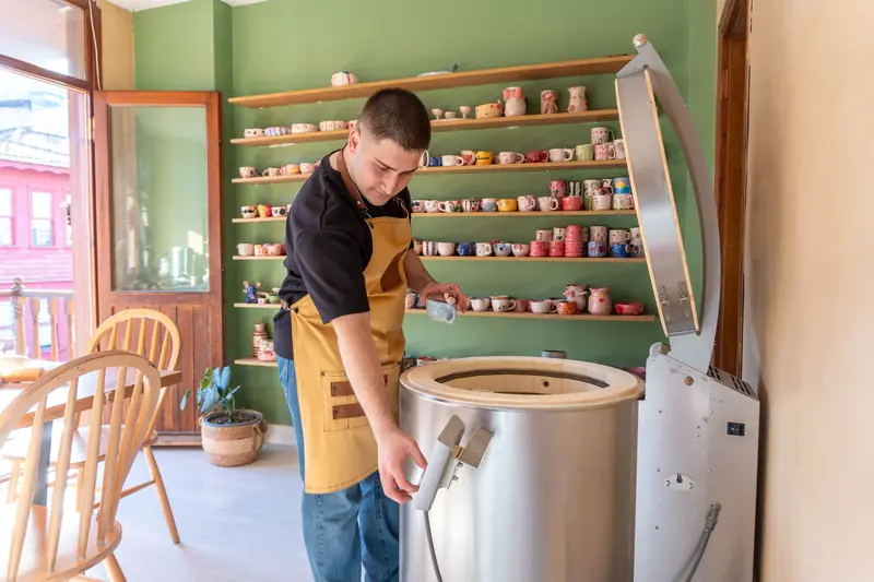 A man working with a kiln in a pottery studio, surrounded by colorful ceramics on display