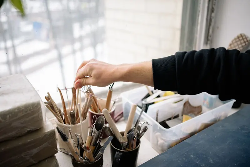 A hand reaching for pottery tools in an art studio, showcasing the craft of pottery making