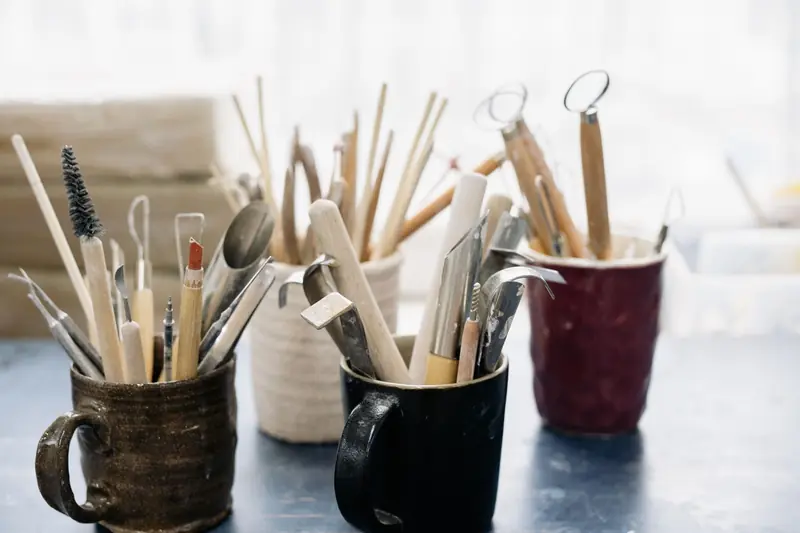 A collection of pottery tools in mugs on a workshop table, perfect for crafting enthusiasts