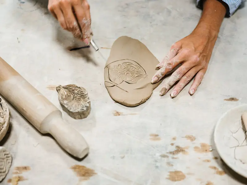 Close-up of hands sculpting clay with detailed stamp pattern on a textured surface