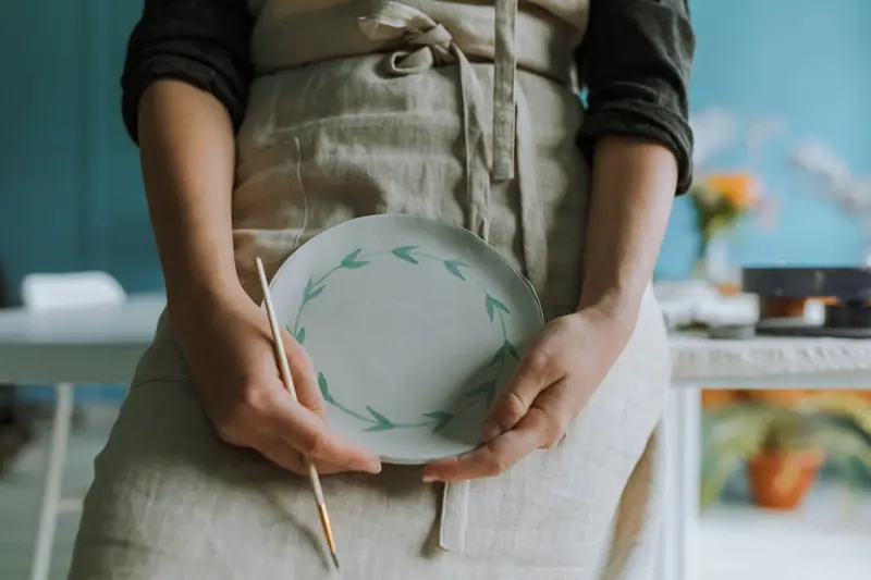 Close-up of an artisan painting a ceramic plate with green leaf pattern