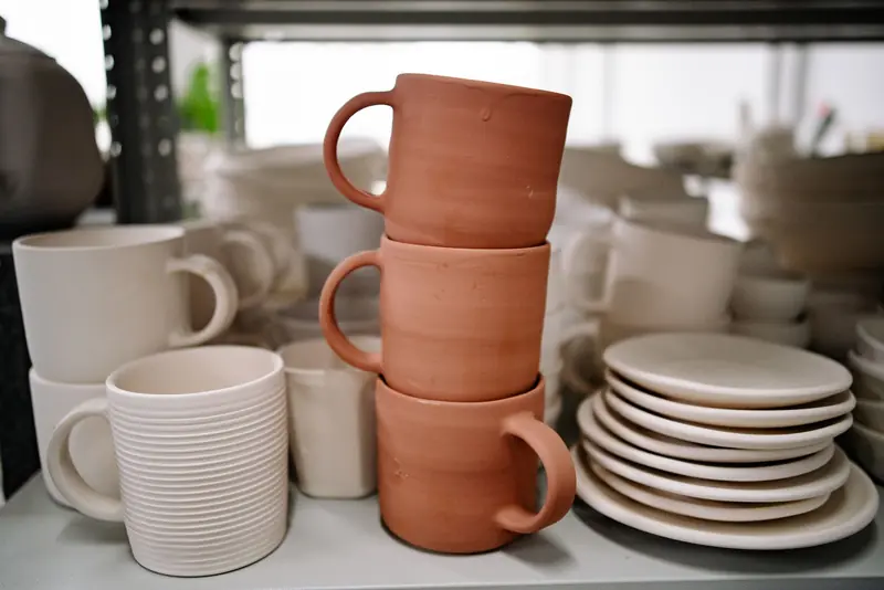 Close-up of stacked handmade ceramic mugs and plates showcasing pottery craft in a studio setting