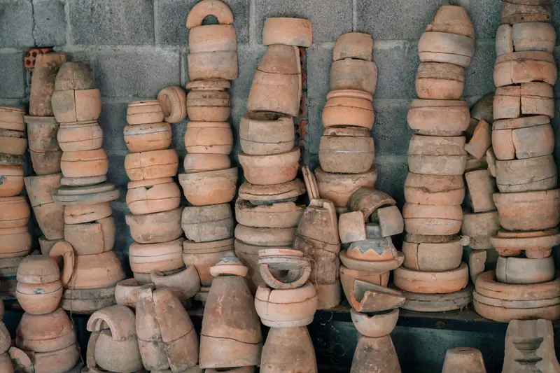 An array of handmade clay pottery pieces stacked against a cement wall, showcasing rustic craft