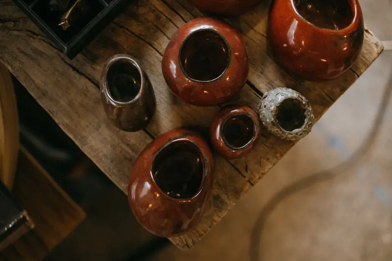 A collection of handmade ceramic pots with rich brown glaze on a rustic wooden table